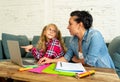 Mother helping young girl doing homework with laptop and school books sitting on the sofa at home in parenting homework and Royalty Free Stock Photo