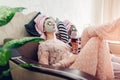 Mother and her adult daughter applied facial masks and cucumbers on eyes. Women chilling while having wine Royalty Free Stock Photo