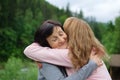 Mother and her adult daughter are hugging spending time together outdoors over landscape of forest and mountains