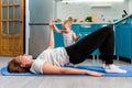 A mother with her baby is doing fitness on a mat in the kitchen. The child stands near the mother`s leg and holds her hand. The Royalty Free Stock Photo