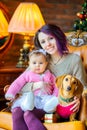 Mother with her daughter and dog sitting in a chair near the festive Christmas tree