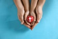 Mother and her child holding heart with cross symbol on light blue background. Christian religion Royalty Free Stock Photo