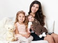 Mother with her children sit in the bed with teddy bear, happy family portrait Royalty Free Stock Photo