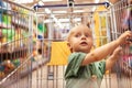 Mother with her cute daughter walking around supermarket, choosing goods and having fun. Little blonde baby girl sits in Royalty Free Stock Photo