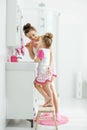 Mother and her daughter brush their teeth with toothbrushes in the bathroom at home. Mom and baby girl in home clothes. Royalty Free Stock Photo