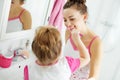 Mother and her daughter brush their teeth with toothbrushes in the bathroom at home. Mom and baby girl in home clothes. Royalty Free Stock Photo
