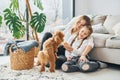 Mother with her daughter playing with dog. Cute little poodle puppy is indoors in the modern domestic room Royalty Free Stock Photo