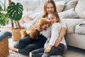 Mother with her daughter playing with dog. Cute little poodle puppy is indoors in the modern domestic room Royalty Free Stock Photo