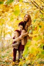 Mother with daughters in autumn park under yellow maples. happy family