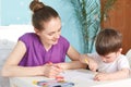 Mother and her five years old son paint with coloutful markers on paper, have interest to art, pose together against domestic inte