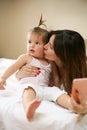 Mother with her little baby having fun in the bed. Using smart p Royalty Free Stock Photo