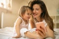 Mother with her little baby having fun in the bed. Using smart p Royalty Free Stock Photo