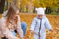 A mother with her little daughter collects leaves in the autumn park.