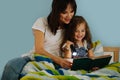 Mother and her little daughter are reading book in bed before going to sleep Royalty Free Stock Photo