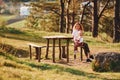 Mother with her little daugter sitting together near wooden table in forest at daytime