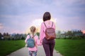 Mother and her little dauther with backpack walking in summer day. View from a back. Royalty Free Stock Photo