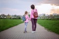 Mother and her little dauther with backpack walking in summer day. View from a back. Royalty Free Stock Photo