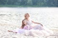 Mother and her little girl enjoying lake view and relaxing on the beach on a sunny day in beautiful dresses. Family lifestyle and Royalty Free Stock Photo