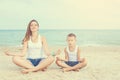 Mother and her son doing yoga on coast of sea on beach. Royalty Free Stock Photo