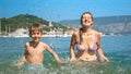 Mother and her son playing and splashing water at the sea beach in slow motion. Family holiday, vacation memories, and