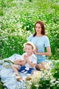 A mother and her son are resting in a field of chamomile flowers. Meditation in the midst of a blooming field. Relaxation and