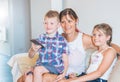 Mother and her sons are watching tv while sitting on a couch at home.Happy mom and her sons on back sofa with TV remote control