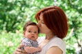 Mother holding in arms infant daughter in striped dress outdoors. Baby girl is a bit scared and looking aside, mom is soothing her Royalty Free Stock Photo