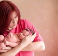 Mother holding in arms newborn daughter in pink hair band and leaning to kiss her baby. Mom and infant child together. Royalty Free Stock Photo