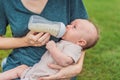 Mother holding and feeding baby from milk bottle in the park. Portrait of cute newborn baby being fed by her mother Royalty Free Stock Photo