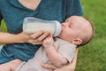 Mother holding and feeding baby from milk bottle in the park. Portrait of cute newborn baby being fed by her mother Royalty Free Stock Photo