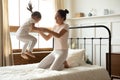 Mother holding hands little daughter while she jumping on bed