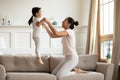 Mother holding hands little daughter while she jumping on couch Royalty Free Stock Photo