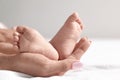 Mother holding her baby`s feet on bed against light background, closeup. Royalty Free Stock Photo