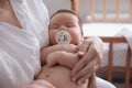 Mother holding her cute little baby with pacifier at home, closeup Royalty Free Stock Photo