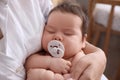 Mother holding her cute little baby with pacifier at home, closeup Royalty Free Stock Photo