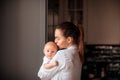 Mother holding her newborn baby standing near the window on the kitchen. Royalty Free Stock Photo