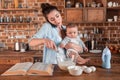 Mother holding her son, talking on smartphone and mixing a dough at the kitchen. family life and multitasking concept