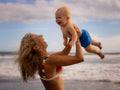 Mother holding and lifting her infant baby boy high in the air on beach. Happy family. Mum and son laughing and smiling. Blue sky Royalty Free Stock Photo