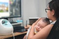 Mother holding newborn baby and working at home, Infant chlid sleeping on the mom chest, Single mom concept