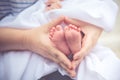 Mother holding newborn tiny and soft skin baby feet in both of hands. Love and affection concept. Maternity and health theme