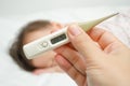 Mother holding thermometer foreground and sick girl in bed