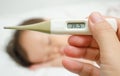 Mother holding thermometer foreground and sick girl in bed