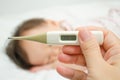 Mother holding thermometer foreground and sick girl in bed