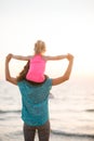 Mother holding young daughter on shoulders at sunset on beach Royalty Free Stock Photo