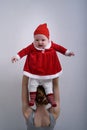 Mother holds a displeased baby in a Santa Claus costume over his head Royalty Free Stock Photo