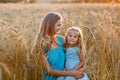 A mother holds her daughter in her arms in a wheat field. A woman and a girl in blue dresses against the background of sunset and Royalty Free Stock Photo