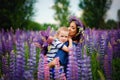 A mother holds her son in her arms in a blooming field of lilac lupine flowers