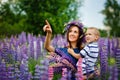 A mother holds her son in her arms in a blooming field of lilac lupine flowers. Shows something in the sky