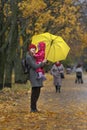 Mother holds a small child in her arms while standing under a yellow umbrella in an autumn park against a background of yellow Royalty Free Stock Photo