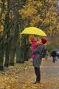 Mother holds a small child in her arms while standing under a yellow umbrella in an autumn park against a background of yellow Royalty Free Stock Photo